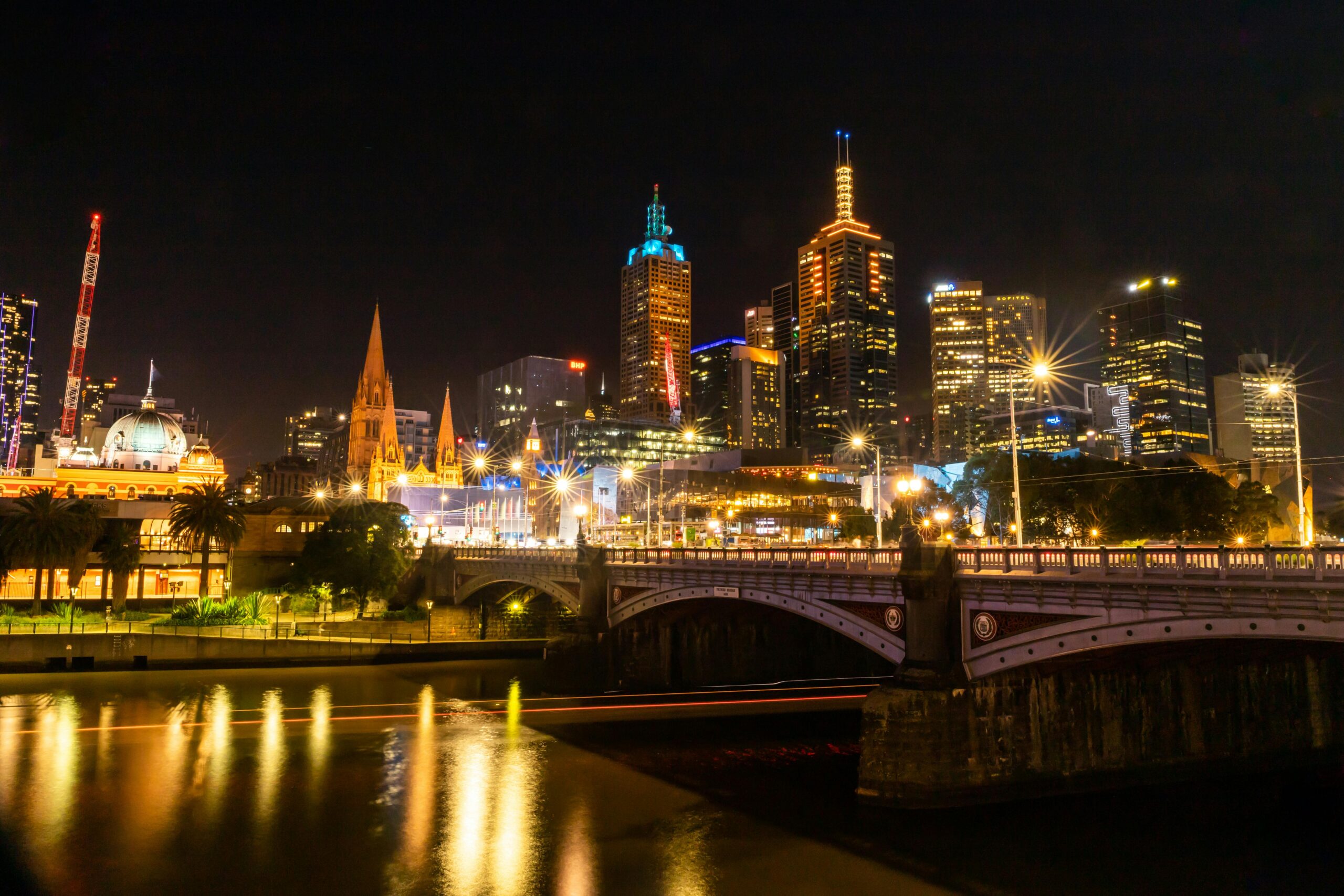Vibrant Melbourne cityscape at night with illuminated buildings and reflections on the Yarra River.